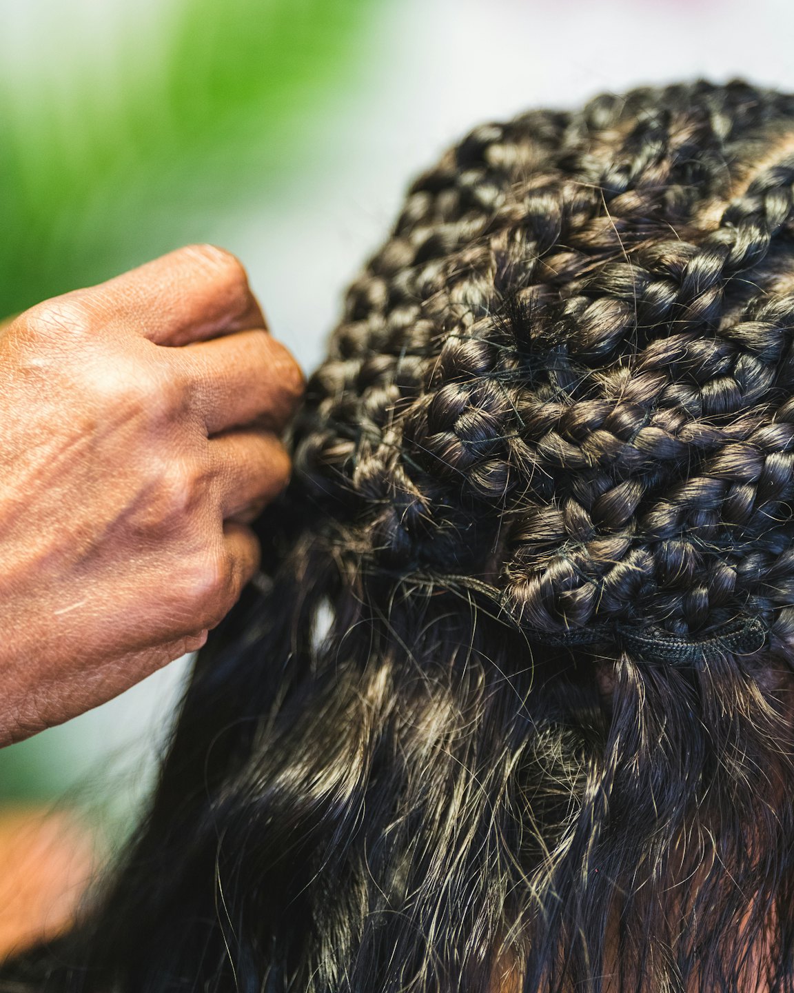 Stylist braiding sections of dark curly hair into cornrows.