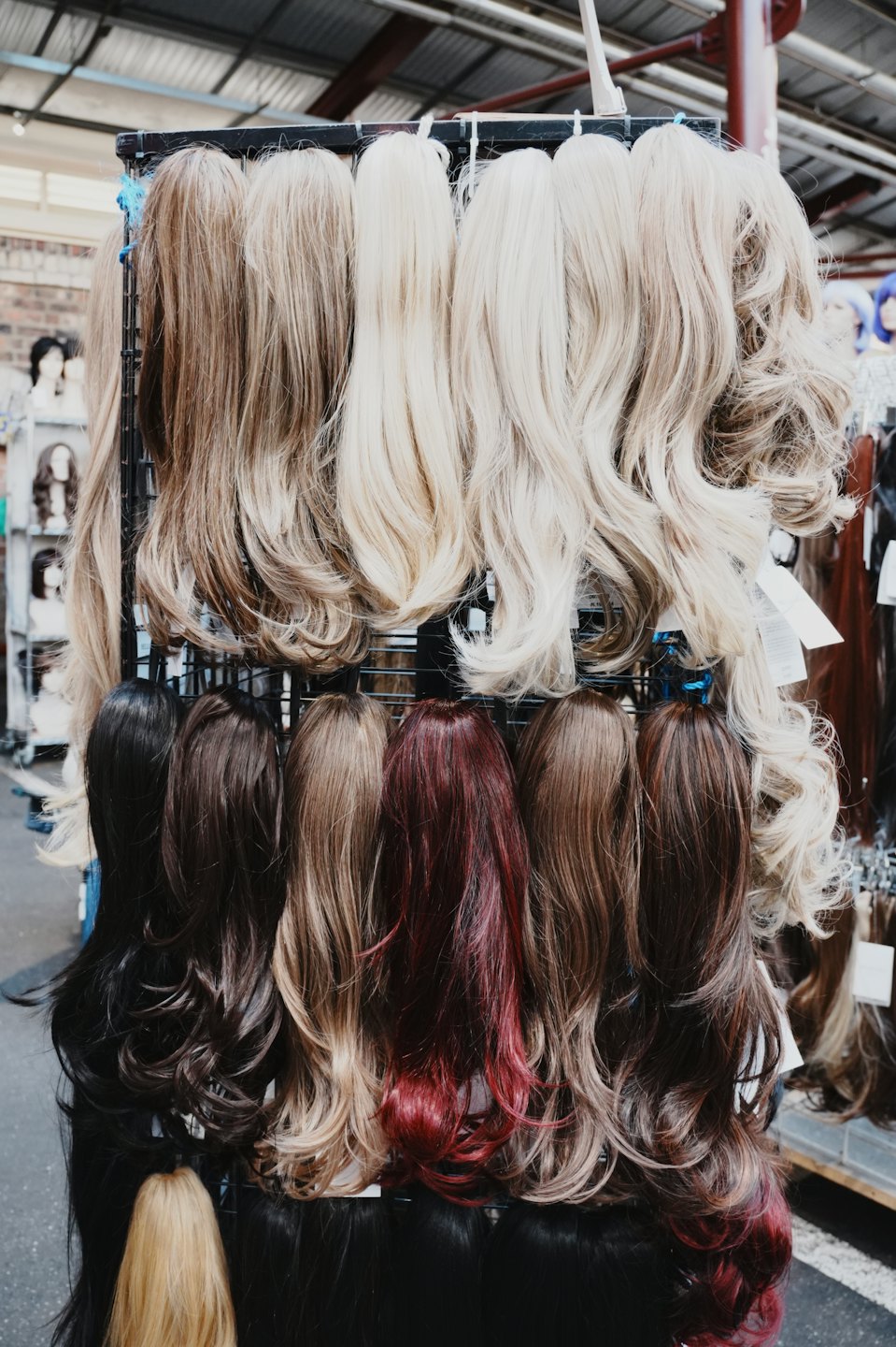Synthetic wigs in various shades hanging on a retail rack.
