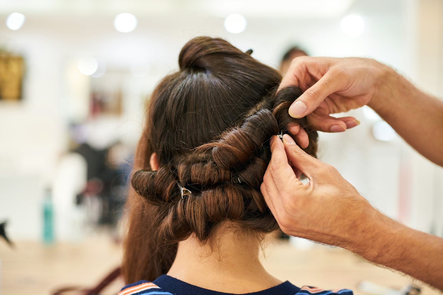Hairstylist's hands curling and pinning long brown hair.