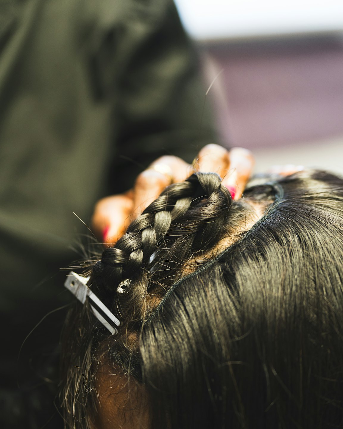 Stylist braiding a client's hair with small white clips.