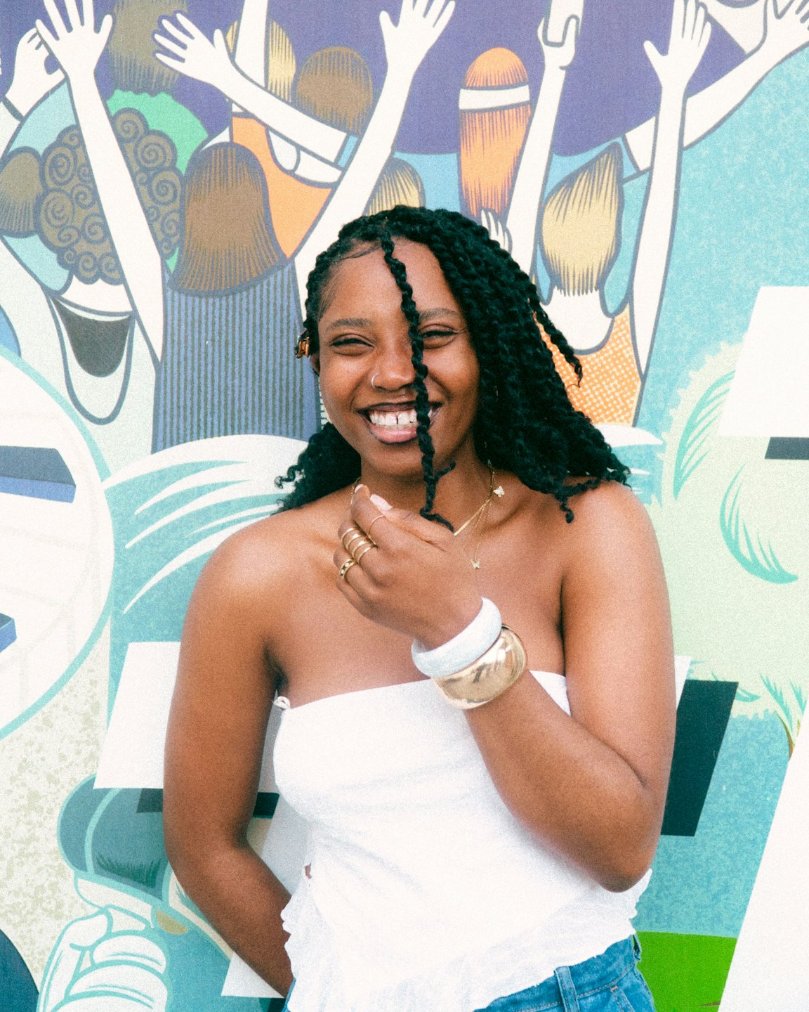 Woman with braided hair smiling in front of a mural.