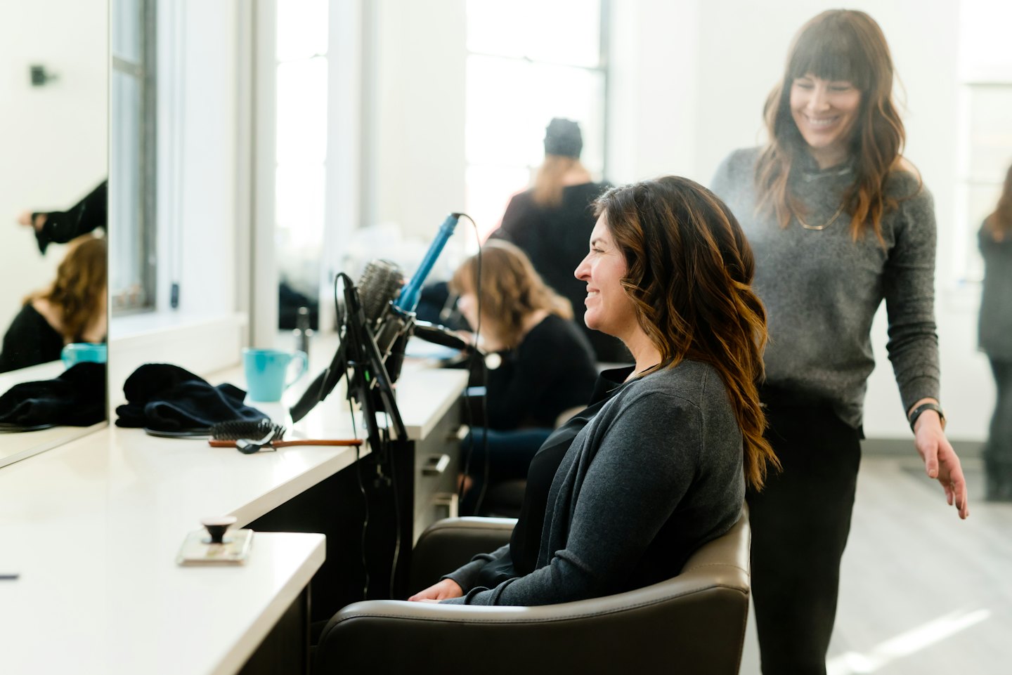 Hairdresser smiles while styling a happy customer's hair.
