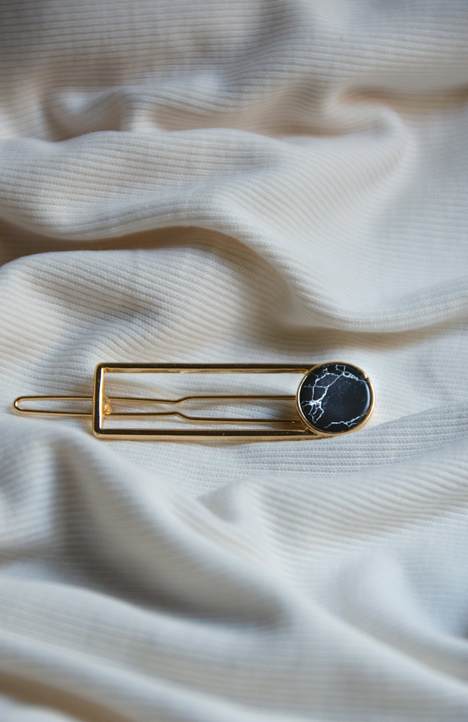 Gold hairpin with marble embellishment on cream fabric.