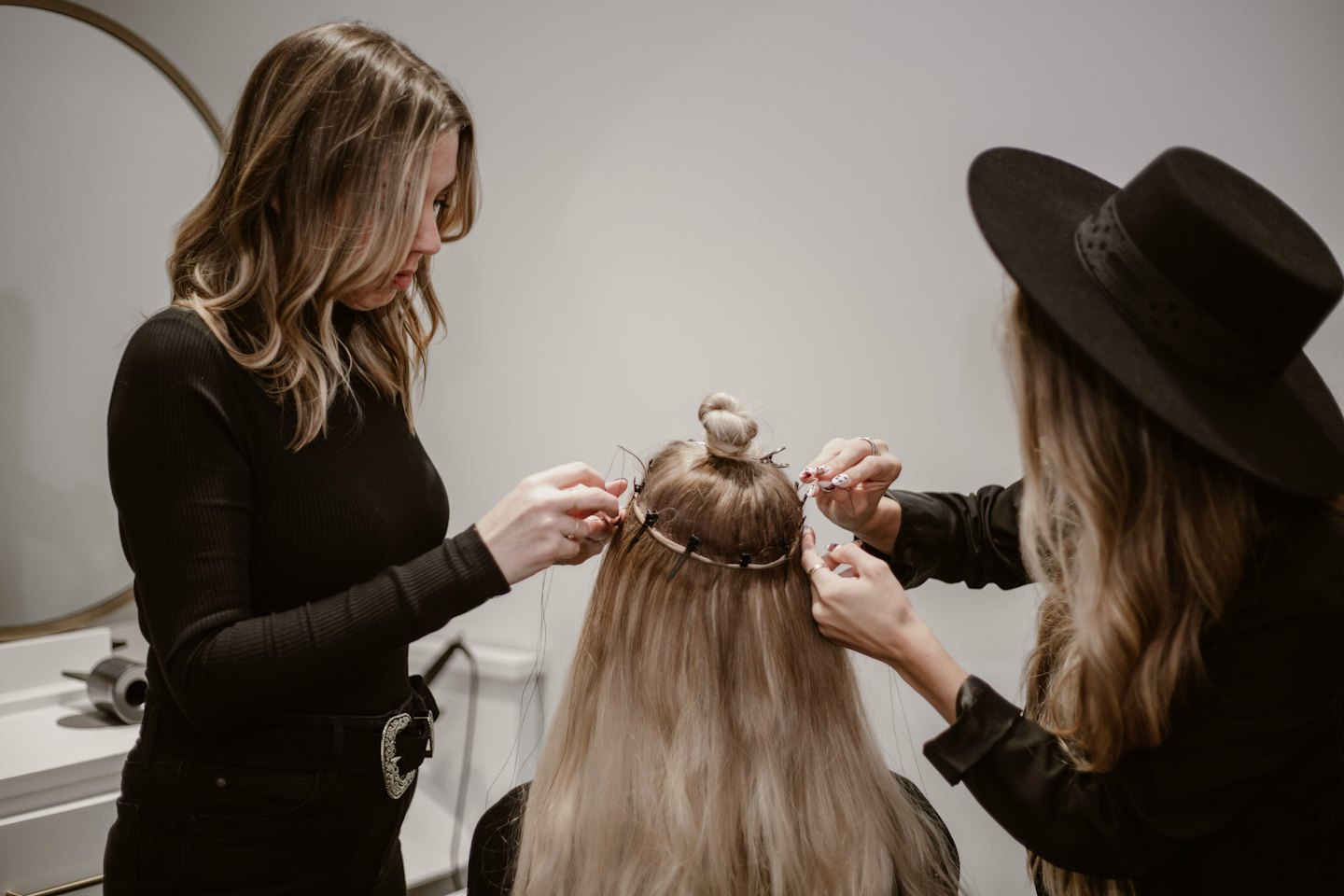 Two stylists installing hair extensions for a client.